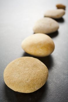 Diagonal straight line of light brown pebbles arranged on dark textured background.