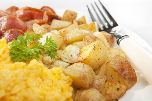 Breakfast of home fries or saute potatoes, with grilled bacon and scrambled egg.