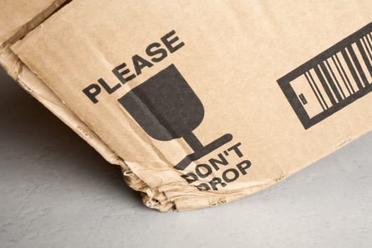 Cardboard box with 'Please Don't Drop' notice dropped on hard tiled floor.