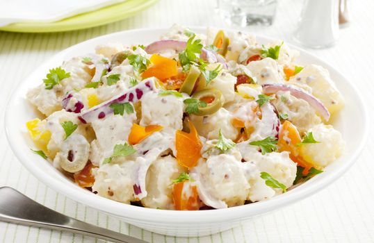 A bowl of potato salad with creamy mustard dressing. Salad also includes orange and yellow peppers, red onions and stuffed olives.