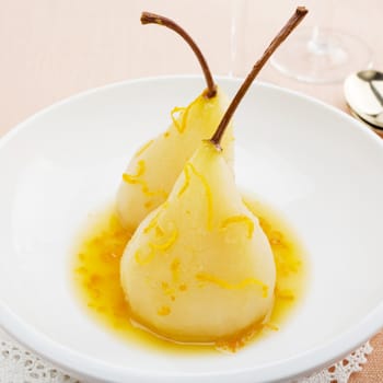 Two pears in a white bowl, poached in orange and lemon juice, garnished with slivers of zest. A delicious healthy dessert, low in calories and fat free.