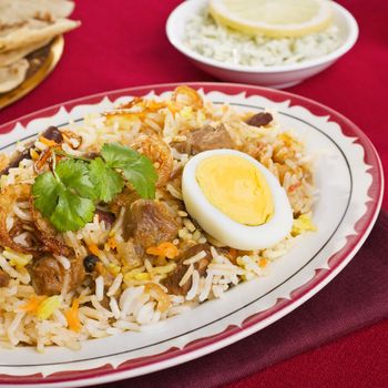 Special occasion Indian curry, lamb biryani with egg, coriander, and red, yellow and white rice.