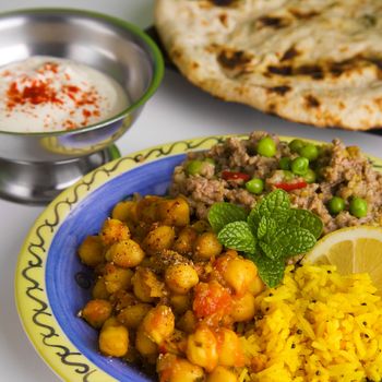 Indian meal of keema matar, masala channa, lemon rice, naan bread and yoghourt, which is minced lamb with peas, spicy chickpeas, yellow rice, nan bread and yogurt. Focus on mint.