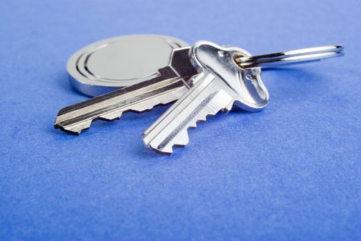 Set of silver coloured house keys on blue texture background. Shallow DOF, focus on end of second key. These are used house keys with a few scratches. Lots of copy space.