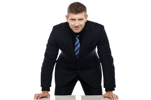 Young businessperson in black suit slightly bending and resting the hands on the desk