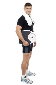 Full length portrait of young male carrying weight scale isolated against white background