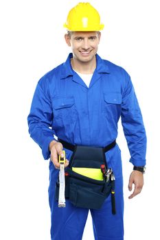 Smart smiling repairman with tools pouch tied to his waist holding measuring tape