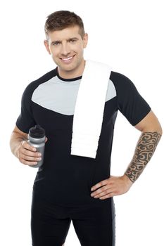 Energetic fit man holding water bottle. Towel on shoulders. Tired after workout