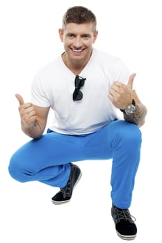 Cheerful young man showing double thumbs up in squatting position isolated against white background