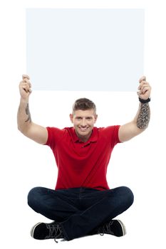 Casual man sitting on floor with billboard raised above head. All over white background
