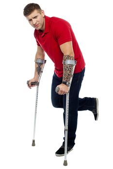 Painful expression of young guy walking with help of crutches. Looking at camera