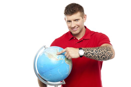 Smiling cool guy holding and pointing at the globe isolated against white