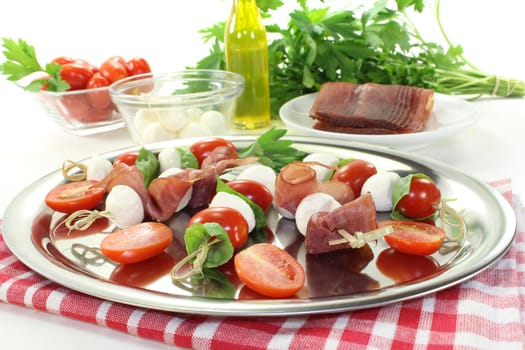 fresh Tomato, mozzarella and ham skewers with basil on a light background