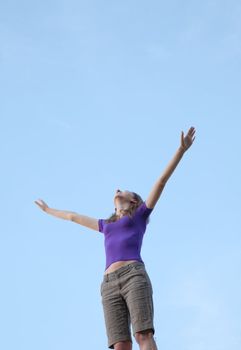 Young woman sitting with raised hand against blue sky