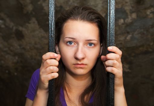 Young woman looking from behind the bars