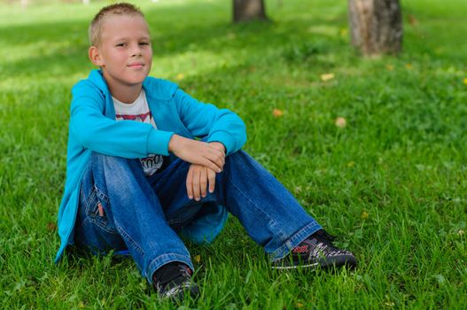 Young boy in jeans sitting on the grass