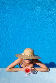 Woman in hat relaxing at the pool with cosmopolitan cocktail