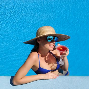 Woman in hat relaxing at the pool with cosmopolitan cocktail