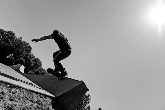 Silhouette of a young skateboarder doing a wall ride trick at the top of the ramp at a concrete skate park. Black and white with high contrast..