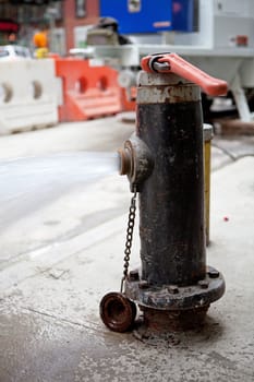 Fire hydrant with valve opened spewing out water onto the street.