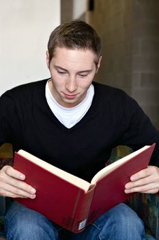 A young college aged man reading a book at the library with a smile.