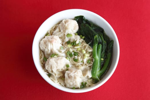 a bowl of noodle and wonton soup on red fabric background
