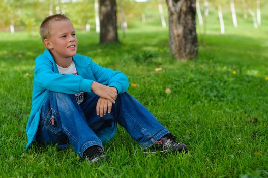 Young boy in jeans sitting on the grass