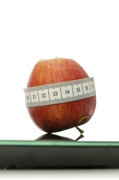 Apple wrapped with measuring tape on a digital scale. Weight loss concept. 