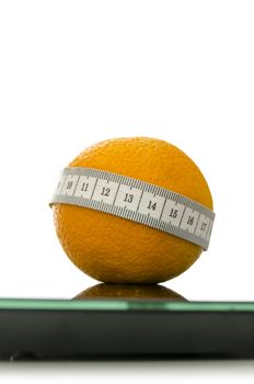 Closeup of orange fruit on a scale wrapped with measuring tape.  Isolated over white background. Weightloss concept.