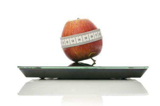 Apple wrapped with measuring tape on a digital kitchen scale. Isolated over white background.Concept of dieting and healthy eating.