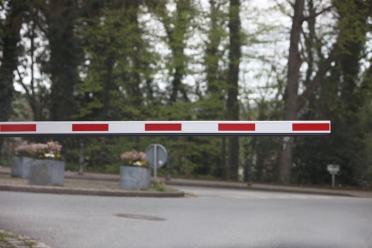 Red and white road traffic barrier or boom in the down position preventing cars from proceeding further until it is lifted again, intersection ahead
