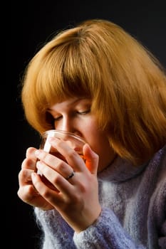 girl in a sweater on a black background drinking tea from a transparent cup. portrait