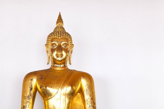 Buddha statue made of stucco and covered with lacquer and gold leaves have been placed in front of the grey wall.