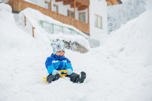 Cute little boy in blue riding on a sled near  the Austrian cottage