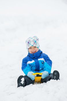 Cute little boy in blue riding on a sled near  the Austrian cottage. Vertical view