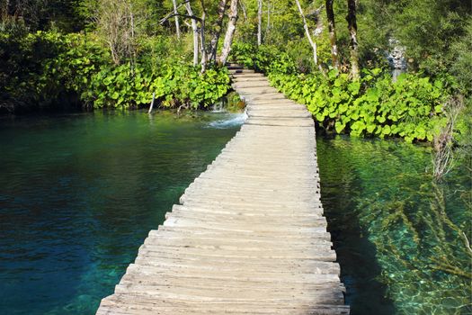 Wooden Path in Plitvice Lakes Park, for crossing over an emerald colored water surface of the lakes. 