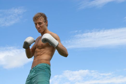 Tough angry guy in boxing gloves, on blue sky background.