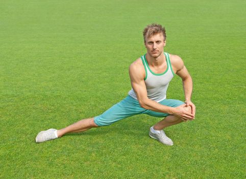 Fit young man exercising outdoors on green field.
