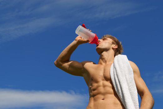 Young athlete with white towel over his shoulder, drinking water.