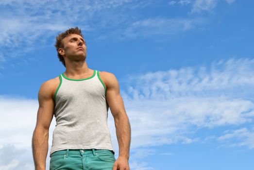 Portrait of a strong young man on blue sky background.