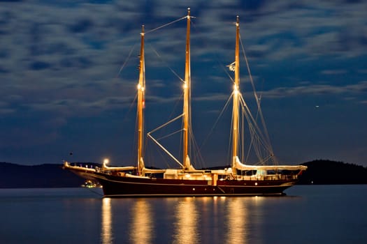 Wooden sailboat illuminated at night anchored