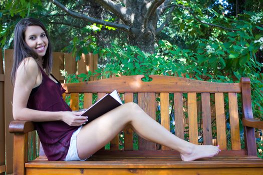 Pretty teen girl reading outside on a bench - copyspace