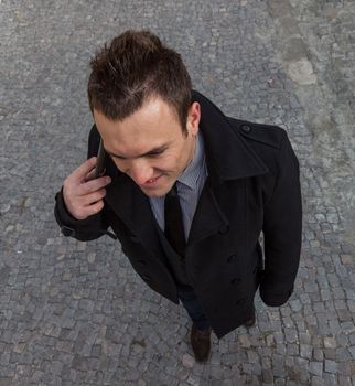 Upper view of a businessman on the phone in a city cobbled street.