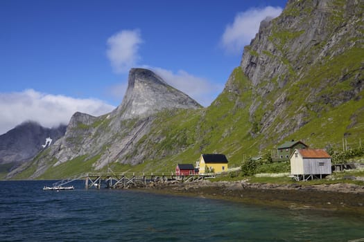 Small norwegian village by fjord near Reine on Lofoten islands, with dramatic mountain peaks towering above
