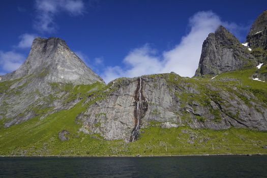 Towering peaks of mountains with waterfall around fjord on Lofoten islands in Norway