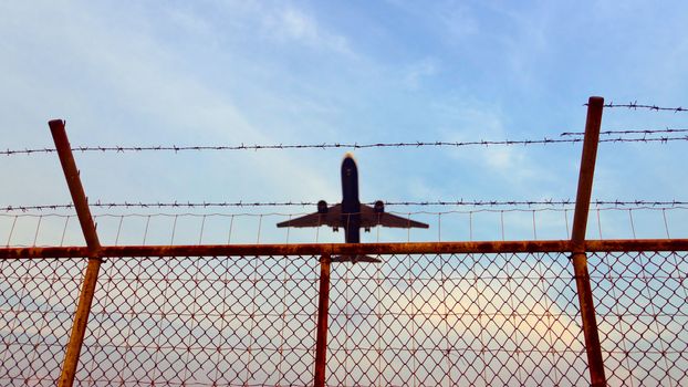 Airplane is flying up over a metal fence