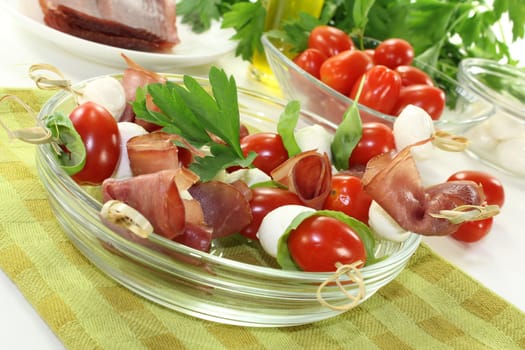 delicious Tomato, mozzarella and ham skewers with basil on a green napkin before light background