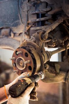 Male hands in gloves use a power tool to clean rust on the wheel hub of a car. In the garage, a man changes parts on a vehicle. Small business concept, car repair and maintenance service. UHD 4K.