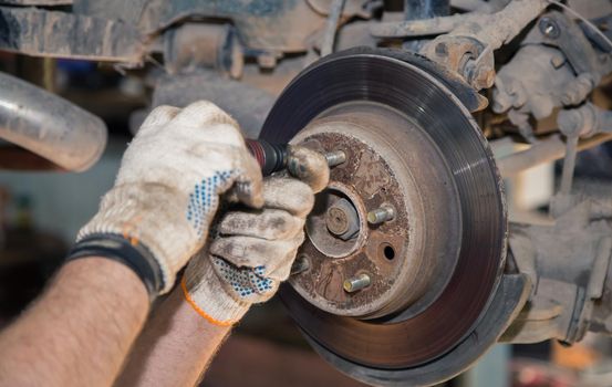 Gloved hands unscrew the rear rusted wheel hub with a screwdriver. In the garage, a man changes parts on a vehicle. Small business concept, car repair and maintenance service. UHD 4K.