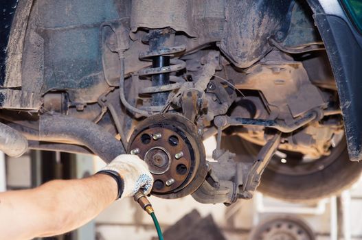 A gloved hand blows compressed air into the rear brake pads of an old car. In the garage, a man changes parts on a vehicle. Small business concept, car repair and maintenance service. UHD 4K.